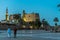 People walking in the square in front of the ancient illuminated Luxor temple at night with dark blue sky and glowing brickwalls