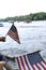 People waving American flags at passing pontoon parade as they sit on edge of dock.