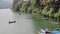 People in wooden boats and catamaran on the lake Phewa on the background of a green wooded shore and boats at the pier at anchor