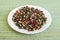 Peppercorn melange. White, black, red and green pepper grains on a white saucer on a green table mat made of natural plant fibers