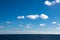 Perfect clouds in blue sky, fluffy clouds in bright sky over ocean. Dark blue calm sea water.