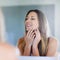 Perfect in every way. a happy young woman examining her flawless skin in the bathroom mirror.