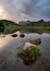 Perfect mountain reflections in water with dramatic sky and rocks in foreground. Taken at Blea Tarn in the Lake District.