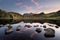 Perfect reflections of a beautiful sunrise with scattered rocks in foreground at Blea Tarn in the Lake District, UK.