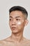 Perfect skincare. Close up portrait of shirtless young asian man with cream applied on his cheek looking aside isolated