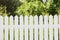 Perfect white picket fence, green garden, trees on background.