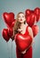 Perfect woman blowing kiss. Pretty girl with red lips makeup and red heart balloons. Fashion model wearing red dress. Love, gifts