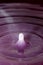 Perfectly formed droplet falling into water with purple reflections