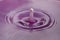 Perfectly formed droplet falling into water with purple reflections