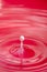 Perfectly formed droplet falling into water with red reflections