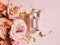 Perfume bottle, pink gold roses and pieces of golden paper on powdery pink background. Top view, flower flatlay