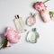 Perfume bottles with flowers on light background. Perfumery, cosmetics, fragrance collection. Flat lay