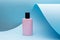 Perfume standing on blue paper background. pink bottle, Modern beauty trend