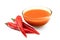 Peri peri chilli sauce in a glass bowl next to three red chillies isolated on white