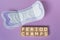 Period cramps text on wooden block. Sanitary pads on purple background.
