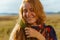 perky laughter on the face of a red-haired girl with freckles who stands in the steppe in an ethnic cape and holds a