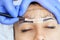 Permanent make-up for eyebrows of beautiful woman with thick brows in beauty salon. Closeup beautician doing tattooing eyebrow.