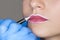 Permanent make-up for lips of beautiful woman in beauty salon. Closeup beautician doing lip tattooing. Face close-up. Make-up and