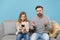 Perplexed bearded man in knitted sweater with child baby girl. Father little daughter isolated on pastel blue background