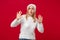 Perplexed shocked young woman in white sweater, hat isolated on red wall background studio portrait. Healthy fashion