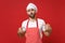 Perplexed young male chef cook or baker man in striped apron white t-shirt toque chefs hat posing isolated on red