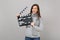 Perplexed young woman in gray sweater, scarf hold classic black film making clapperboard isolated on grey background