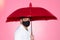 Persian businessman with mask holding umbrella against pink wall