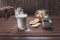 Person adding sugar into the glass of milk on a rustic wooden table with cookies and cinnamon powder