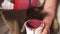 Person adds thick red paint to container for decorating