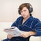 Person in big ear-phones on sofa reads newspaper