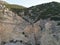 Person on a big rock cliff with bushes and the sky in the background.