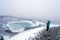 Person with blue jacket ovelooking ice covered Viti volcanic crater near Krafla geothermal area in Iceland.
