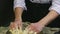 Person in chef uniform by hands slowly kneads soft yeast dough in metal bowl