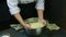 Person in chef uniform quickly kneads soft dough with raisins in big deep metal bowl