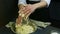 Person in chef uniform slowly kneads soft dough with raisins in big deep metal bowl