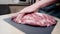 a person cutting a piece of raw meat on a cutting board. A woman cuts pork with a knife