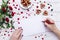 Person drawing on a white paper with a red pencil near heart-shaped cookies with rose petals