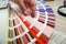 Person with a finger shows to the selected color in the palette for paint tinting. Colored catalog fan