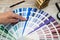 Person with a finger shows to the selected color in the palette for paint tinting. Colored catalog fan