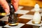 Person fingers with black pawn making move on chess board.