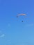A person flying a orange paraglider in the blue sky.