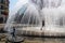 Person in a fountain in a public park surrounded by buildings and vehicles under sunlight