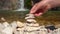 Person during a halt on the bank of mountain river on hiking trip tries to collect pyramid of stones, but everything