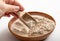 Person hand holding wood spoon and picking Psyllium husk flour powder from wood bowl indoors at home.