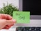 Person hand sticking a green paper note with the reminder Tax Day on it on to a monitor at an office workplace