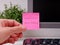 A person hand sticking a pink paper note with the reminder Password 12345678 on it on to monitor at an office workplace