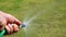 A person hand watering green grass with a hose