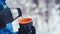 Person hands in black knitted gloves holds thermos and cup with tea.