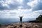 A person hands up standing on rocky mountain looking out at scenic natural view