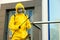 Person in hazmat suit with disinfectant sprayer cleaning metal railing on city street. Surface treatment during coronavirus
